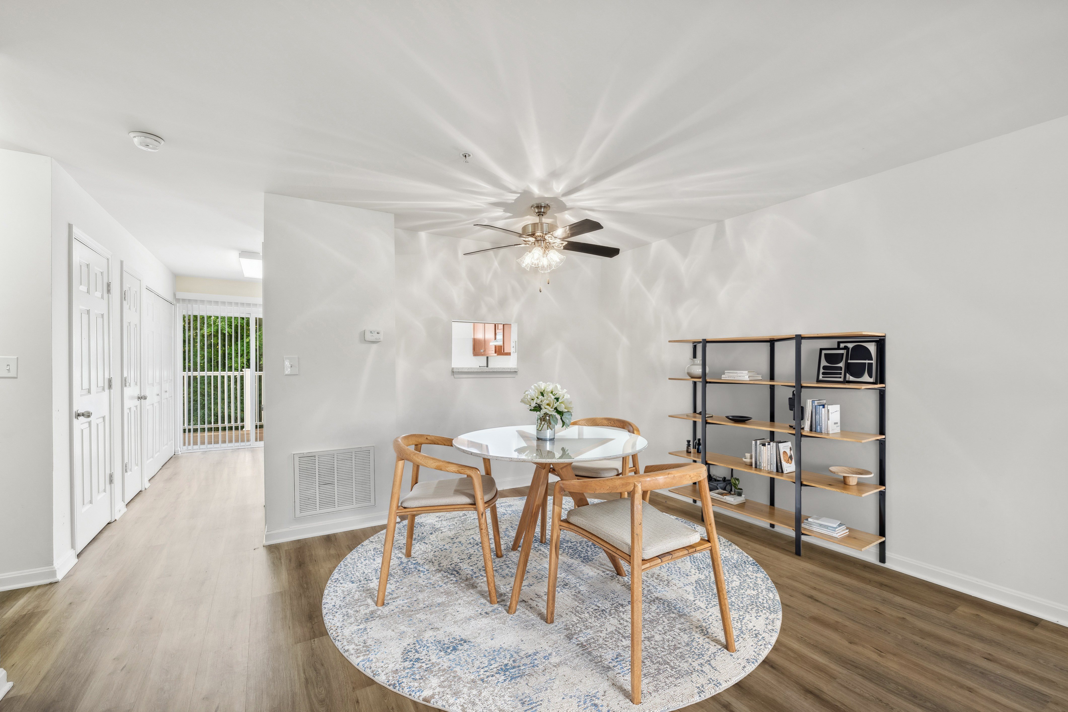 A dining room with a round table and chairs, a ceiling fan, and a rug on the floor.